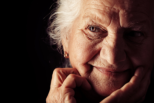 Focused lighting on elderly woman resting her face in her hands smiling, dark background